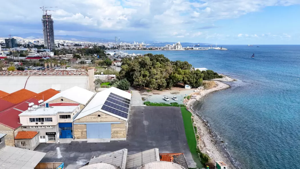 Aerial view of VIMA Art Fair’s venue in Limassol, Cyprus, showing a renovated warehouse with solar panels near the shoreline, overlooking the Mediterranean Sea.