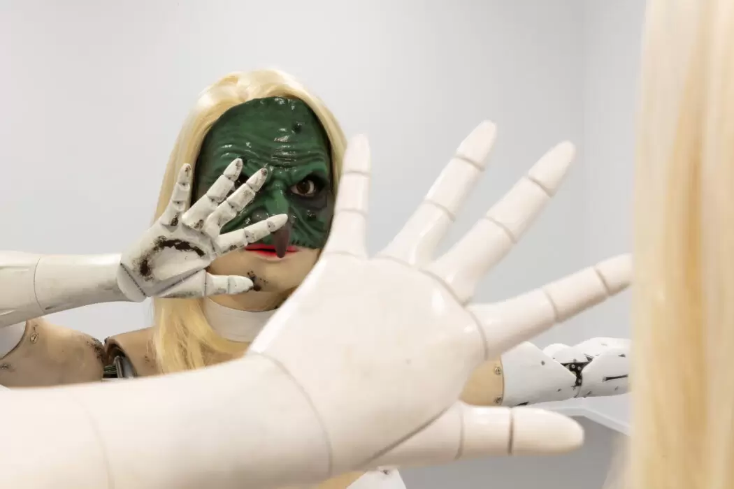 Jordan Wolfson, Female Figure (2014), mixed media sculpture of a blonde female figure with robotic arms and a green mask, raising her hand toward the viewer. © Jordan Wolfson. Courtesy of the artist and AMA Collection. Installation view by Sebastiano Pellion di Persano.