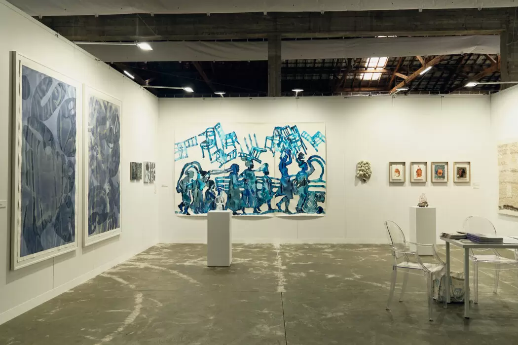 Art fair booth by NIKA Project Space at VIMA 2025, featuring large abstract blue paintings, small framed works, sculpture on pedestals, and minimalist furnishings.