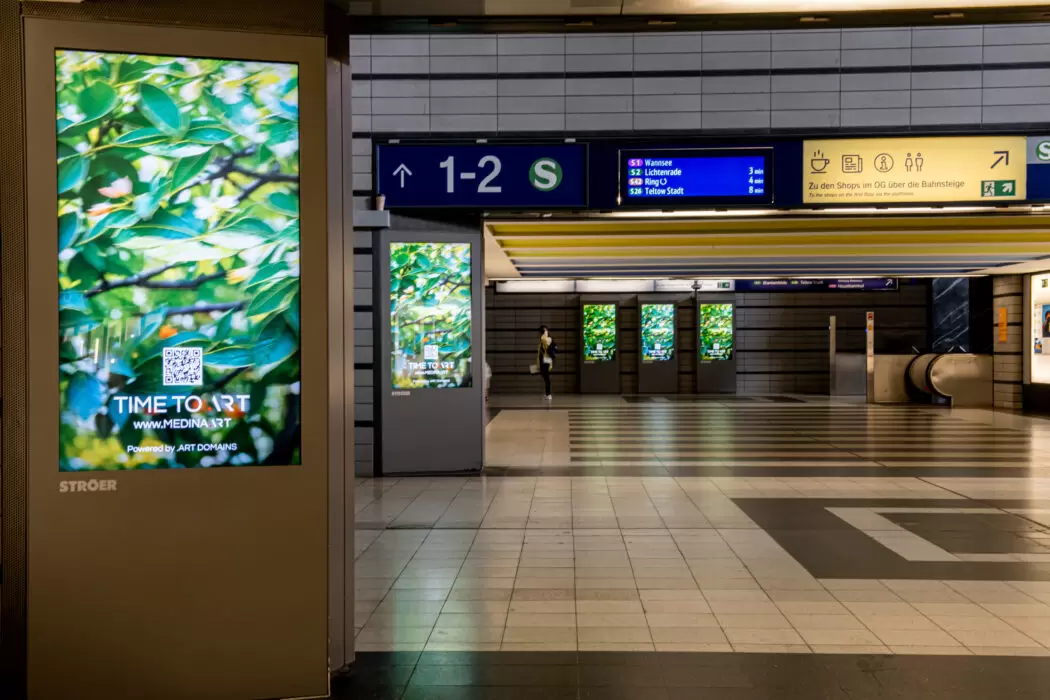 Multiple digital screens inside a Berlin subway station display Medina Kasimova’s TIME TO ART artwork with vivid green leaves, replacing ads with art during Berlin Art Week.