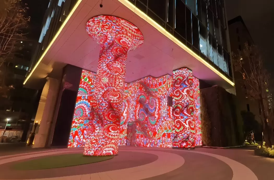 A nighttime view of Cromwell’s generative artwork Scarlet Symphony: Dragon’s Awakening projected across the curved exterior walls and columns of Taipei Lumitree, glowing with intricate red and orange patterns that ripple across the building.