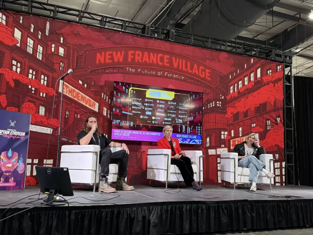 Panel discussion on art and Web3 at ETHDenver’s New France Village stage featuring Rob McCarty, Nadia Taiga, and Elena Zavelev seated on stage in front of the red ETHDenver backdrop.